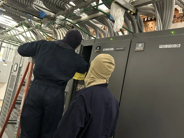 New Phase Electrical technicians in arc-flash PPE servicing a Vertiv DC power distribution cabinet at an Arizona critical facility